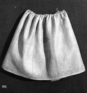  Black and white photo of a full, gathered skirt with textured fabric, displayed against a dark background.