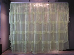  "Kjøkken" by Ingunn Bakke, an art installation featuring a series of overlapping sheer pastel green curtains made from synthetic fibers, machine-sewn into a plain weave, softly illuminating in artificial light against a neutral backdrop, embodying a serene and airy visual motif.