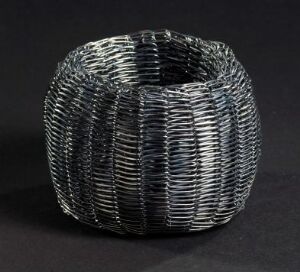  An oxidized silver bracelet titled "Nøste" by Toril Bjorg, featuring a textured design reminiscent of a yarn ball, with multiple ribbed bands wrapped closely together, displayed against a black background.