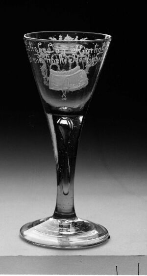  Black and white photo of an ornate glass goblet with a decorative band featuring a relief of figures around its upper section, set against a plain background.