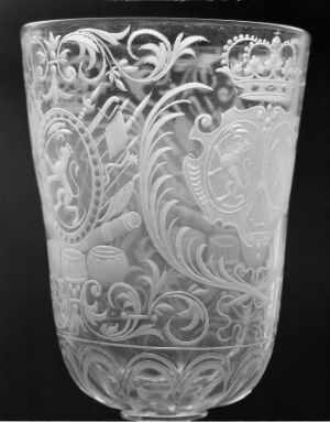  An intricately etched or engraved clear glass vessel with ornate Baroque-style foliage and scrollwork patterns, featuring a central shield-like motif, displayed against a neutral background.