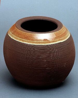  A hand-thrown ceramic pot with a dark brown textured exterior and a gradient rim of toasted almond, sand, and earthy orange on a light to medium gray background.