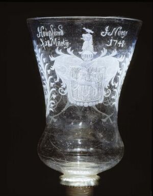  An intricately etched clear glass goblet with a tulip-like shape, featuring the name "Jan van der Heyden" and the year "1714" above an engraved coat of arms, showcased against a dark background.