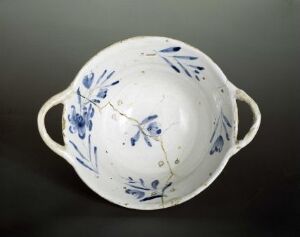  A white porcelain bowl with blue floral patterns and two handles, set against a dark background.