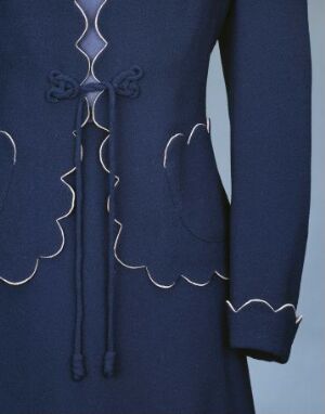  Close-up of a navy blue garment with white accent stitching and decorative symmetrical loops and a bow-like design near the collar area.