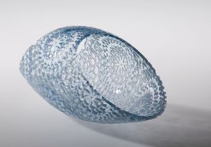  "Objekt nr. 7 (blå)" by Kari Håkonsen, a sandblasted and perforated glass object with delicate lace decoration, exhibiting a complex blue lace-like pattern on an oval, semi-translucent glass body with varying hole sizes on a white background.