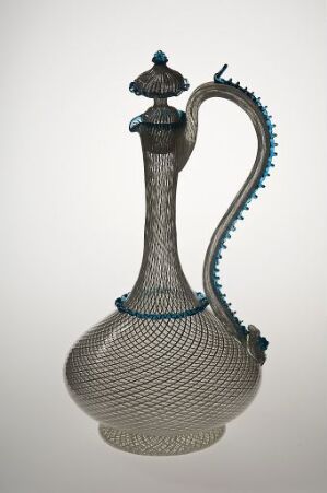  An intricately textured ewer or pitcher with a metallic body featuring fine linear detailing and a spiraling ridge adorned with turquoise embellishments, extending from the lid to the base, against a neutral background. Artist Name and Title: Unknown.