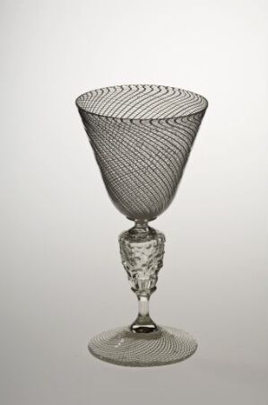  A transparent glass goblet with an intricate helical line pattern on the bowl, faceted stem with a central knob, and a stable circular base against a light grey background.