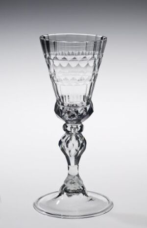  An elegant, transparent glass goblet with ornate stem detailing, set against a light grey background.