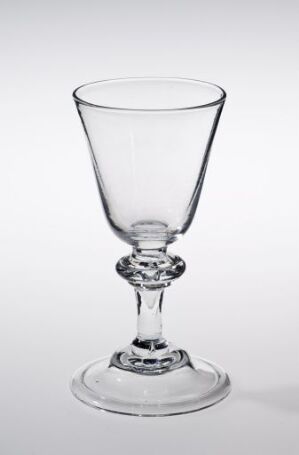  An elegant clear glass wine goblet with a decorative stem, set against a light gray background.