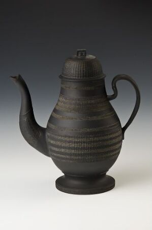  A traditional dark matte black ceramic teapot with horizontal ridges on a gradient background, featuring a curvy spout and a sturdy handle with a fitted lid on top.