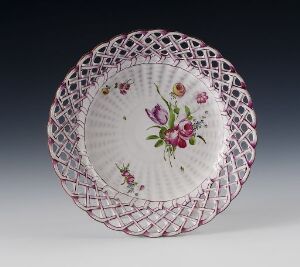  A decorative plate with a reticulated rim in light pink and a central floral design featuring purple and pink flowers with green leaves, set against a graded dark to light background.