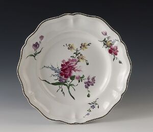  An ornate ceramic plate featuring a hand-painted floral design with deep pink and violet flowers at the center, surrounded by smaller sprigs and set against a white background with scalloped edges.