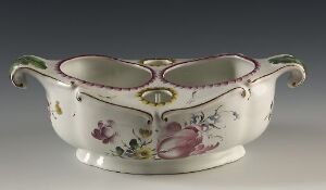  A dual-compartment, off-white porcelain sauce boat with gold trims and hand-painted floral designs in purple, pink, and green, set against a neutral grey background. Artist name and title are unknown.