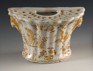  An ornate ceramic object with a flared shape, embellished with intricate gold patterns on a creamy base, set against a dark background.