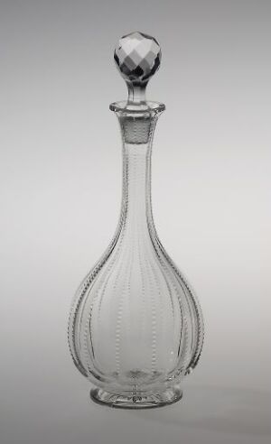  Clear glass decanter with a slender neck, vertical ridges, and a multifaceted stopper set against a light gradient background.