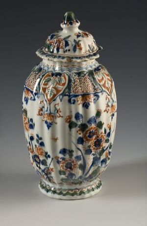  An ornate porcelain jar with a lid, featuring cobalt blue, orange, and green floral motifs on a white background, with heart-shaped handles and a decorative finial.