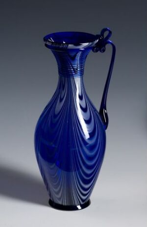  An elegantly shaped deep cobalt blue vase with a white swirling pattern, broad base, slender neck, wide mouth, and a single handle, set against a neutral gray background.