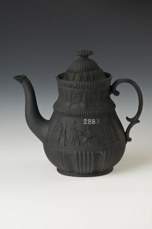  An ornate black teapot with textured patterns and a rounded lid, featuring a long curved spout and dramatic handle, marked with raised numbers "2983" on the front, against a light grey background. Artist name and title are unknown.