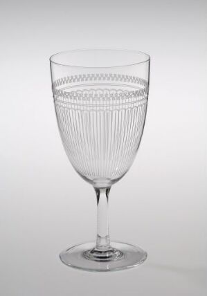  A clear, patterned wine glass with a finely detailed upper half and smooth lower half, standing upright on a light gray background.