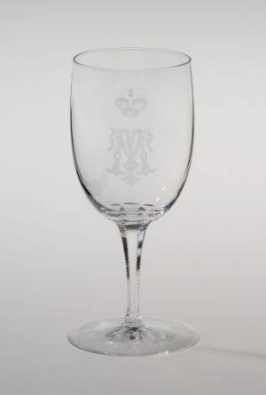  A clear glass goblet by Hadeland Glassverk with an engraved monogram set against a white background, showcasing a sanded decorative band and an intricate, sanded and engraved design on the bell-shaped bowl, a slender stem, and a flat, stable base.