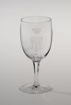  A clear glass goblet with engraved emblem from Hadeland Glassverk against a light grey background, showcasing a blown glass design with a slender stem and stable base, featuring intricate cut and engraved decorations.