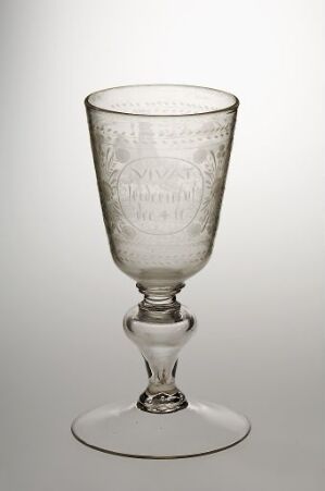  A transparent goblet with intricate engravings stands on a graduated grey to white background, embodying classic elegance and skilled glass craftsmanship.