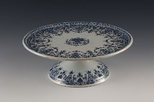  An ornate blue-and-white porcelain compote or cake stand with intricate floral designs, displayed against a gradient gray-to-black background.