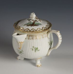  An ornate porcelain teapot with a cream base color, embellished with a landscape scene, floral decorations, and gold accents, including a scalloped pattern on the lid's edge and detailed motifs on the handle and spout.