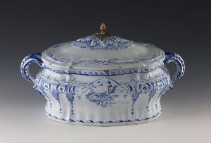  An oval-shaped porcelain tureen with a cobalt blue floral pattern on a white base. It has two handles, a matching patterned lid with a golden knob on top, and is presented against a neutral gray background. Artistname and title are unknown.