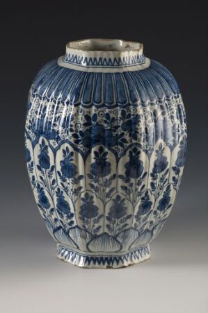  An intricately patterned ceramic vase with cobalt blue and white designs, featuring floral motifs, vertical striped patterns, and leafy borders, all highlighted by a glossy finish.