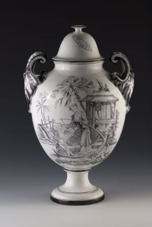  A decorative ceramic urn with a glossy white finish and greyscale pastoral scenes, featuring ornate handles and a detailed illustration of a gazebo surrounded by trees. The urn has a classical shape with a matching lid on top, photographed against a plain gray background.