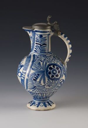  A traditional blue and white ceramic pitcher with a metal handle and intricate patterns, set against a neutral gray background.