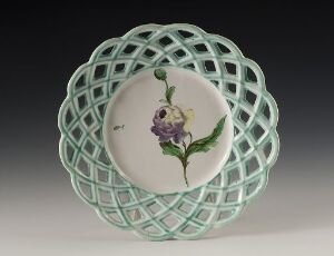  A finely crafted ceramic plate with a pastel mint green lattice edge and a central white circle featuring a painted purple pansy with green leaves, against a gradient background fading from white to dark gray.