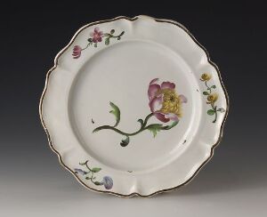  A vintage ceramic plate with scalloped edges, featuring hand-painted floral motifs in pink, yellow, purple, and green on an off-white base, set against a neutral gray background.