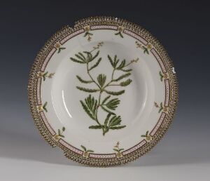  A feldspar porcelain plate by Den kgl. Porcelainsfabrik with a glossy white base, decorated with a gold chain-link pattern around the rim, and a hand-painted green foliage design in the center, set against a gray backdrop.