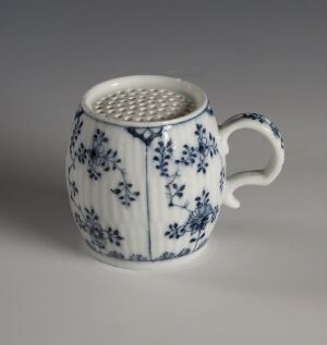  A small white ceramic mug with intricate blue floral patterns and a perforated top, possibly a spice grater, sits against a light background.