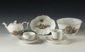  A porcelain tea set on a light background, including a teapot, two cups with saucers, and a large serving bowl, all with a sepia-toned pastoral design.