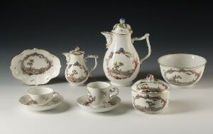  An antique porcelain tea set displayed against a neutral background, featuring a teapot, milk pitcher, sugar bowl with lid, a single cup with saucer, an additional saucer, a serving bowl, and a large oval platter, all with matching floral designs and gold trim.