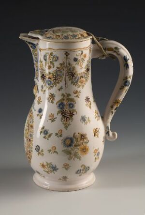  An antique ceramic pitcher with a cream base color, adorned with hand-painted floral patterns in soft yellows, deep blues, burnt oranges, and dark browns with hints of greenery and golden accents, against a neutral grey background. Artist name and title are unknown.