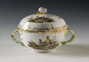  An exquisitely painted oval porcelain soup tureen with a floral-topped lid, pastoral scenes around its body, ornate gold accents, and elegantly curved handles, set against a soft gray background.