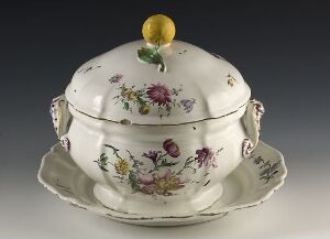  An intricately painted porcelain soup tureen with floral designs and a lemon-yellow finial situated on a matching underplate against a gradient gray background.