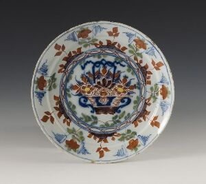  An intricately designed ceramic plate with a central blue, yellow, and red floral motif set against a white background, surrounded by smaller brown and green floral patterns on the rim.