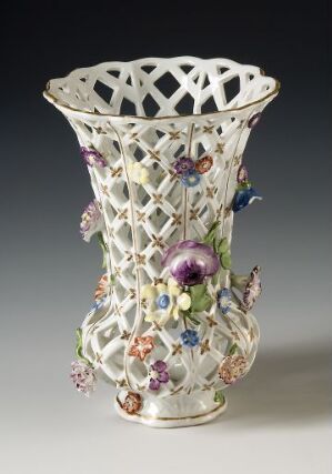  An intricately designed porcelain vase with a lattice pattern and hand-painted flowers in shades of purple, pink, yellow, and green against a white background.