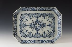  An octagonal ceramic platter decorated with intricate blue and white floral designs, featuring a central flower flanked by successive rings of botanical motifs and outer lattice borders, on a gray background.