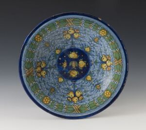  A handcrafted ceramic bowl with a deep cobalt blue interior, decorated with yellow flowers, green leaves, and blue circular motifs on a soft grey background.