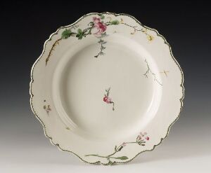  An elegant porcelain plate with a scalloped edge, decorated with a delicate pattern of pink flowers and green leaves against a creamy white background, set against a neutral gray to white gradient backdrop.