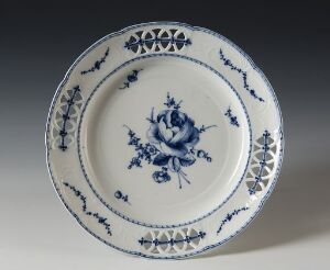  A traditional porcelain plate featuring a cobalt blue and white color scheme, with a central floral design and intricate geometric and floral patterns along the rim. The plate is displayed against a subtle gray background with a gentle shadow to one side, emphasizing the detailed artwork.