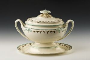  A traditional cream-colored ceramic sugar bowl with handles and a decorative lid, set on a matching saucer with a subtle decorative band, displayed against a neutral background.