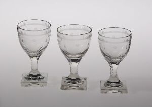  Three empty clear glass goblets in varying sizes, arranged in a row on a light background. Each goblet has a curved bowl, a short stem, and a square-shaped base.